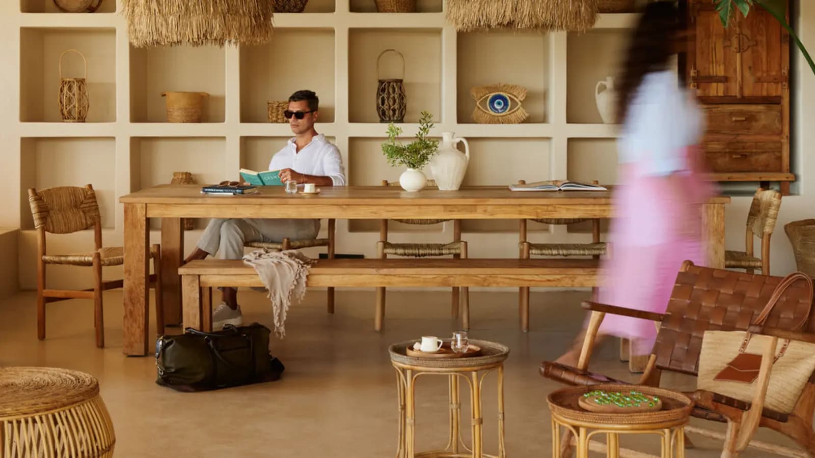 Hotels.com Find Your Perfect Somewhere poster showing a guest seated at a wooden table in a warm resort interior with a blurred figure passing through the room.