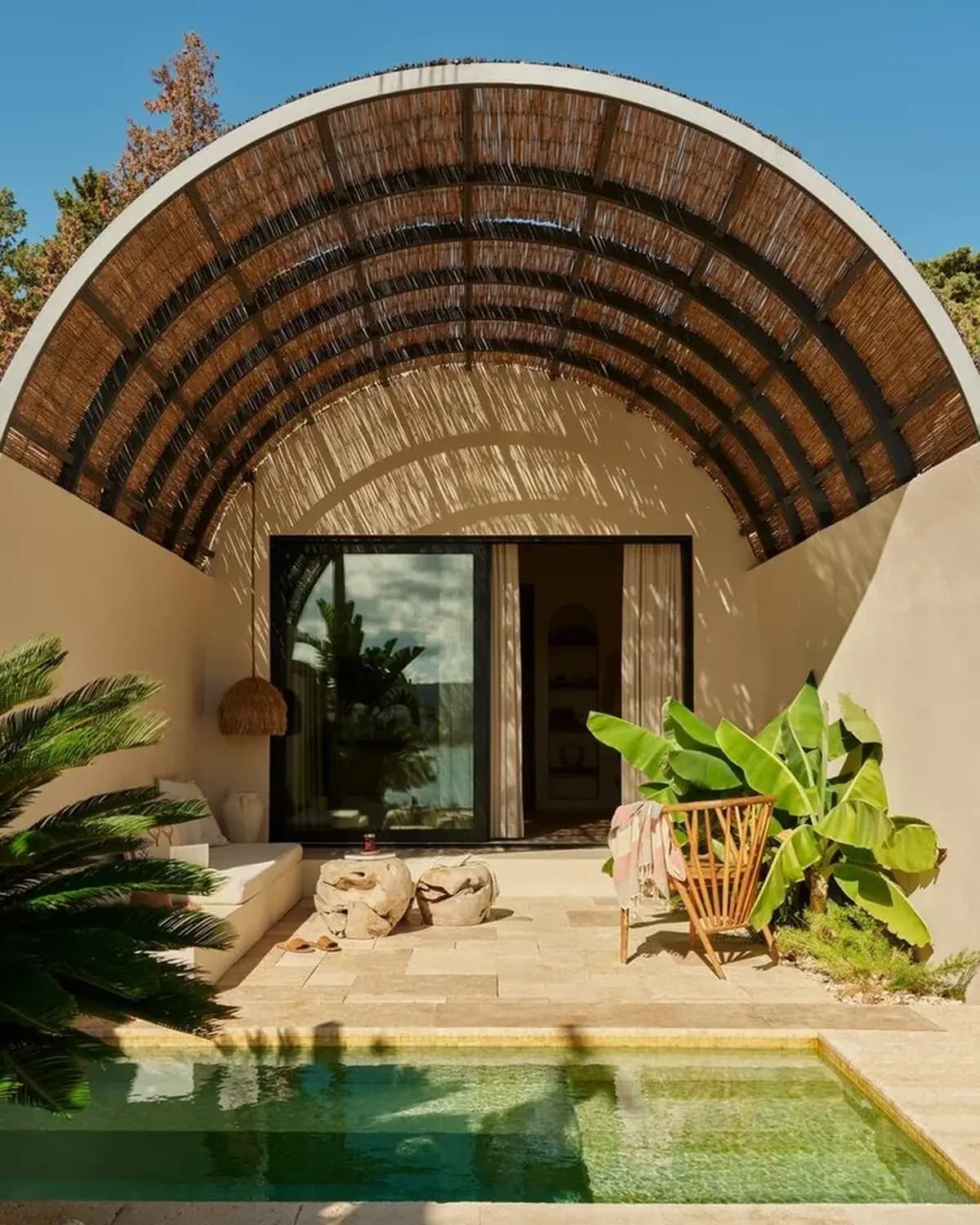 Expedia That Feeling poster showing a sunlit resort terrace with a pool, lounge furniture, plants, and arched shade canopy.