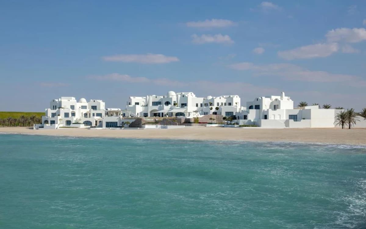 White beachfront architecture in Abu Dhabi with turquoise sea, sandy shore, palm trees, and clear sky.