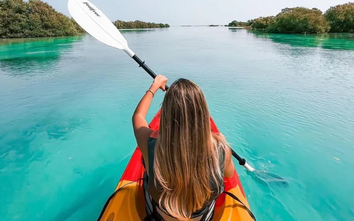 Kayaker moving through turquoise Abu Dhabi mangrove waters with low islands and calm open channel.