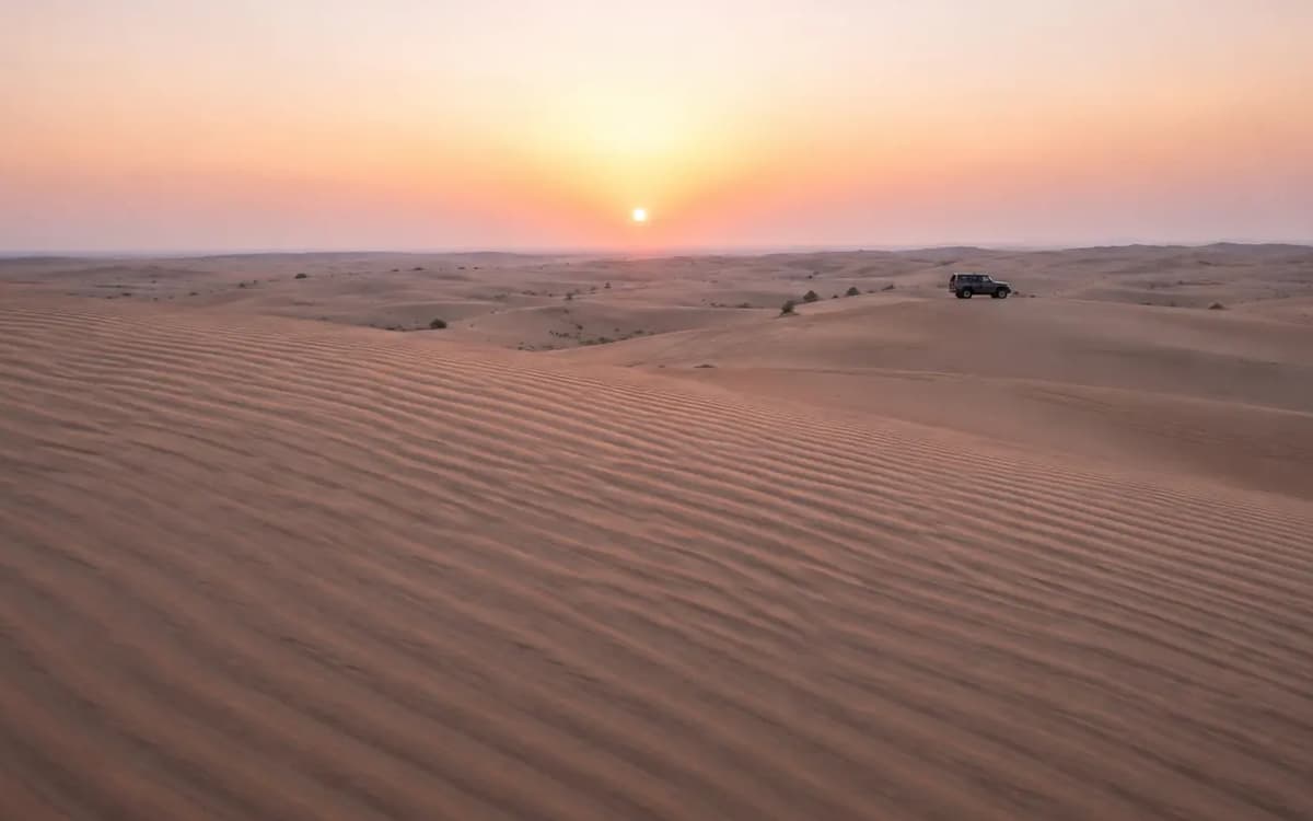 Abu Dhabi desert dunes with rippled sand, soft shadows, distant mountains, and dramatic clouded sky.