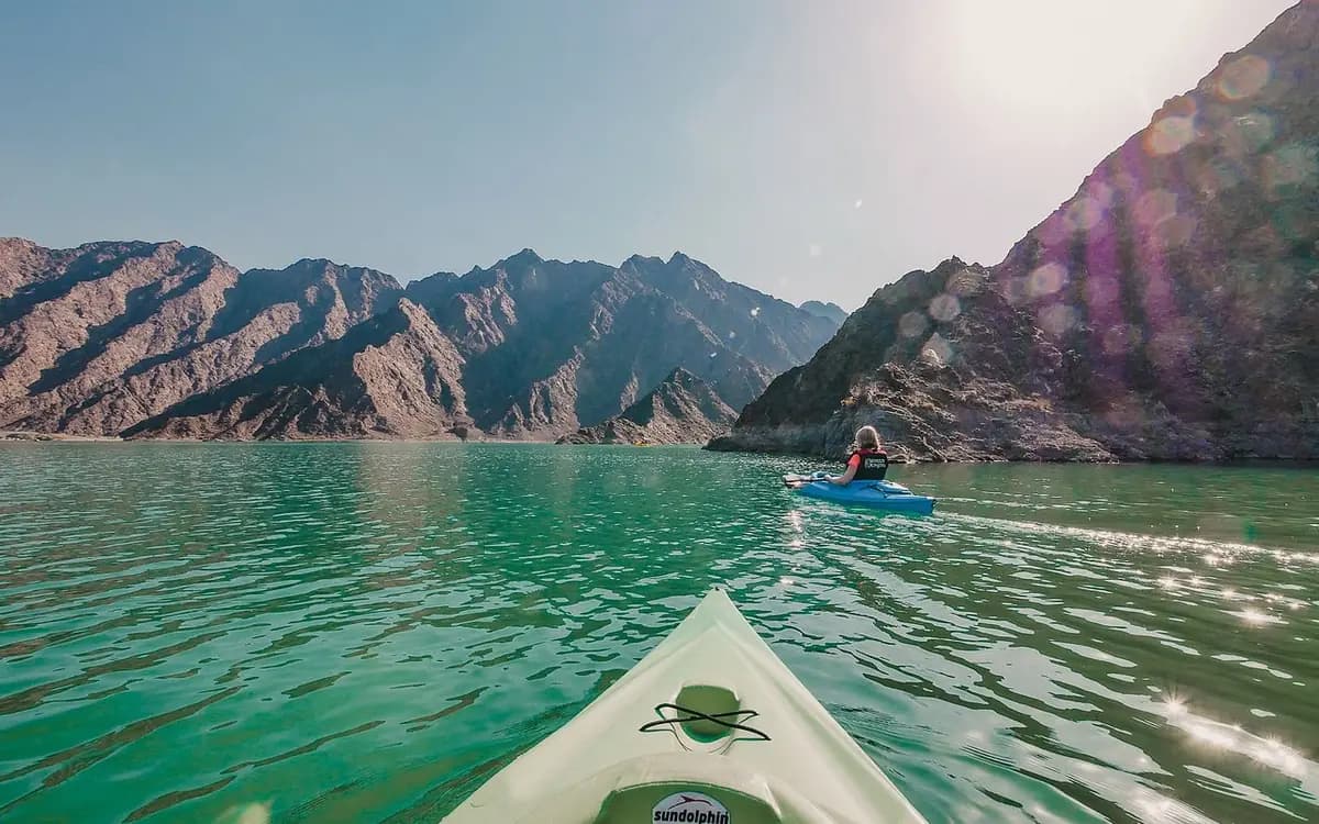 Kayakers on Hatta Dam in Dubai with turquoise water, rocky mountain slopes, and bright sunlight.