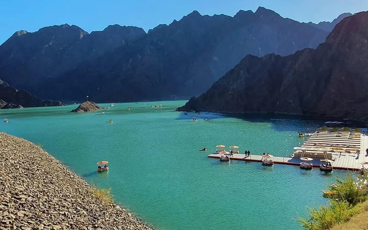 Hatta mountain dam landscape with turquoise water, rocky peaks, floating platforms, and mountain resort setting.