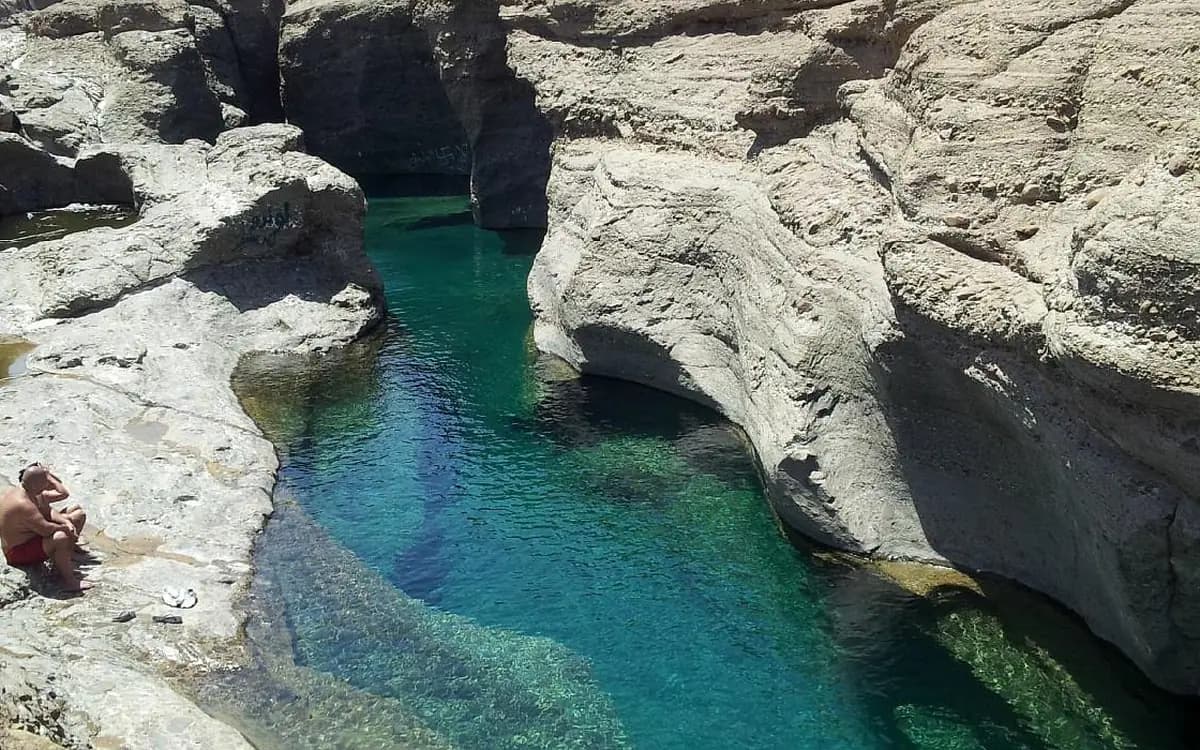 Rocky wadi pool in Hatta mountain terrain with clear turquoise water, stone cliffs, and dry peaks.