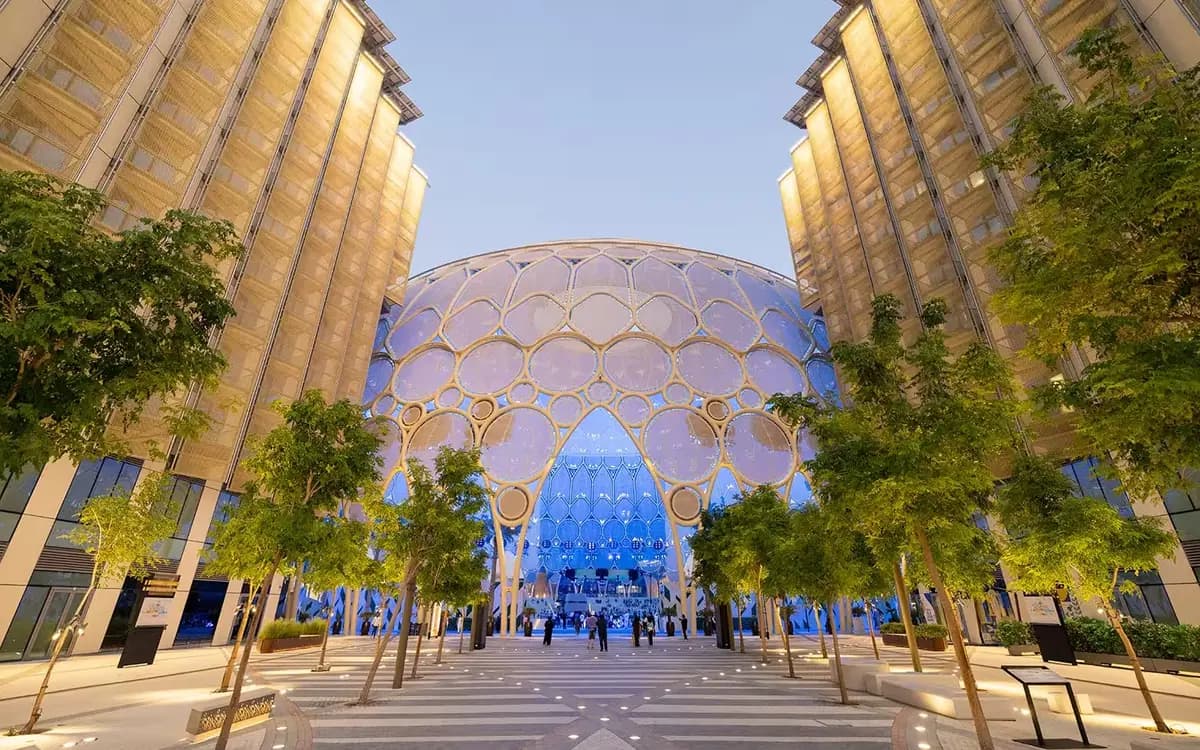 Expo City Dubai entrance plaza with illuminated dome architecture, trees, walkways, and modern public space.