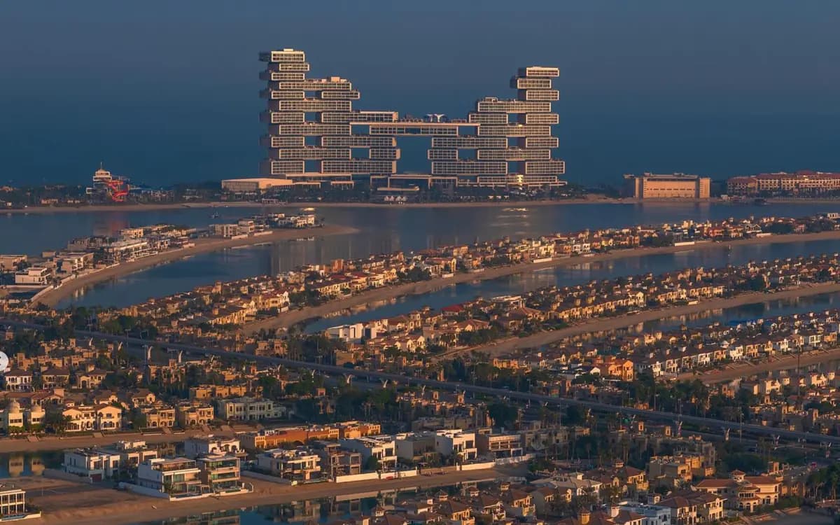 Palm Jumeirah aerial view with villas, waterways, beach coastline, and landmark resort architecture at golden hour.