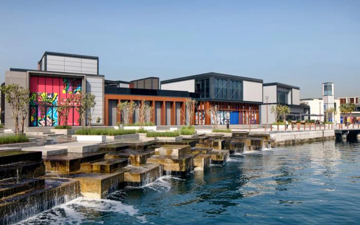 Dubai Creek promenade with contemporary waterfront buildings, colourful facade, stepped water features, and calm water.