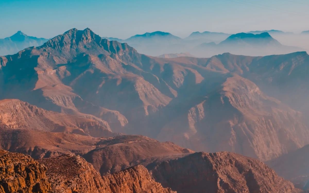 Ras Al Khaimah mountain landscape with layered rocky peaks, deep valleys, and warm haze.