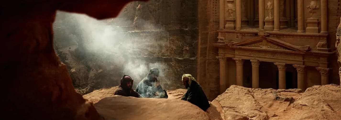 Travelers seated above the Petra Treasury with smoke, sandstone cliffs, and carved heritage architecture in Jordan.