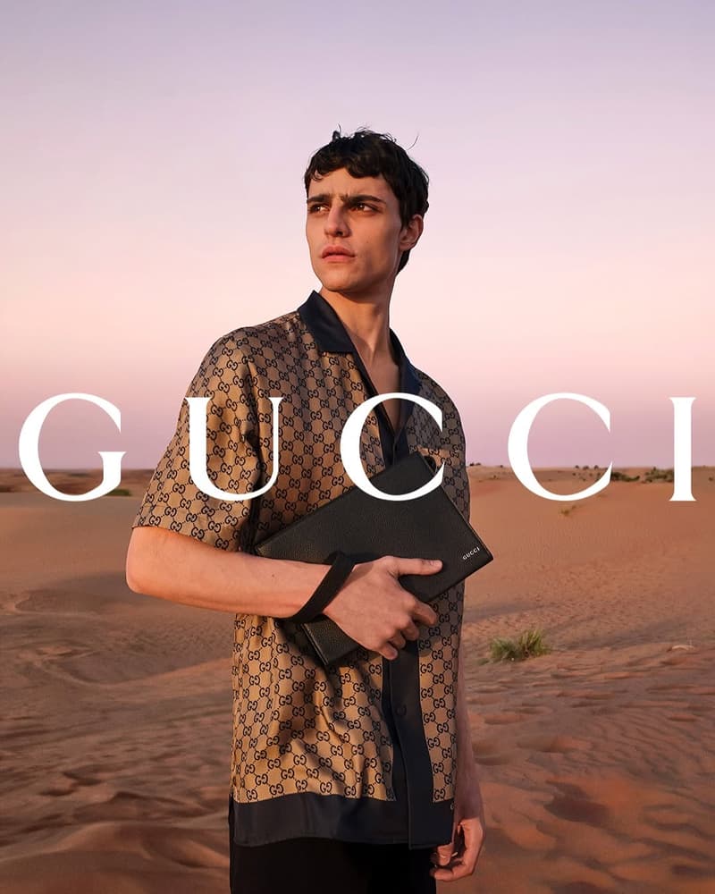 Fashion campaign image in the Sharjah Desert with male talent, desert dunes, evening sky, and visible brand wordmark.