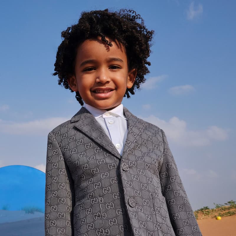Young fashion talent in a patterned suit standing on a Sharjah Desert set with blue sky and sand in the background.