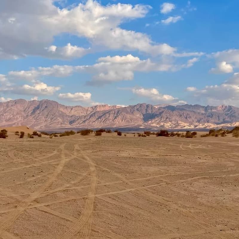 Large desert dune with rippled sand, rocky formations, pale sky, and open remote terrain.