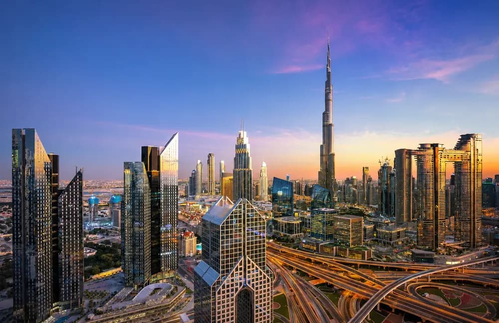 Dubai skyline at sunset with Burj Khalifa, high-rise towers, roads, and warm evening city light.