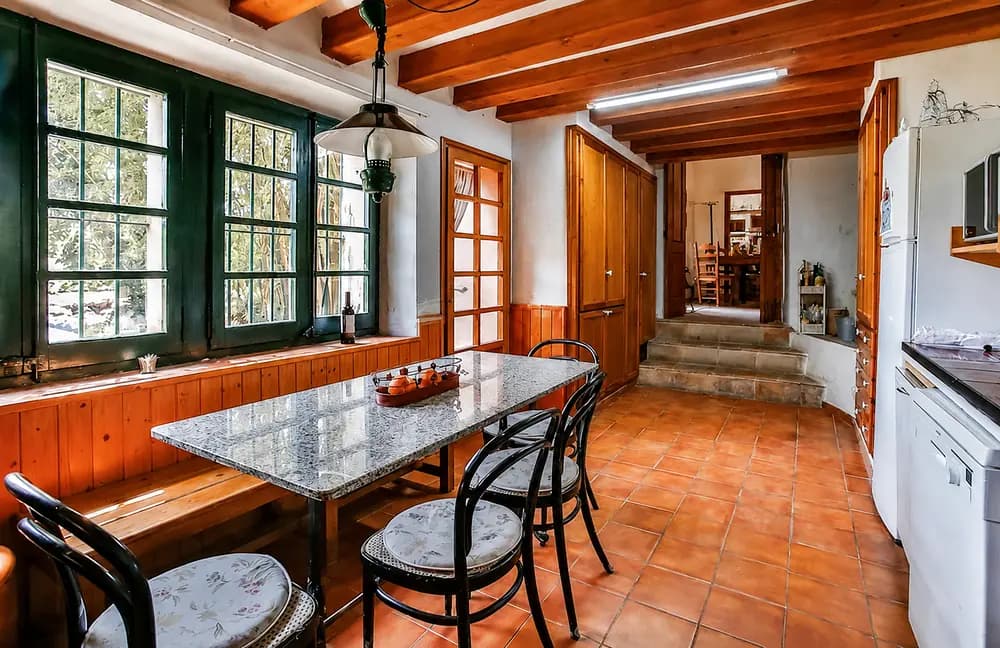 Rustic kitchen and dining room at Cosido Farm in Tarragona with green windows, wooden beams, terracotta floor, and table.