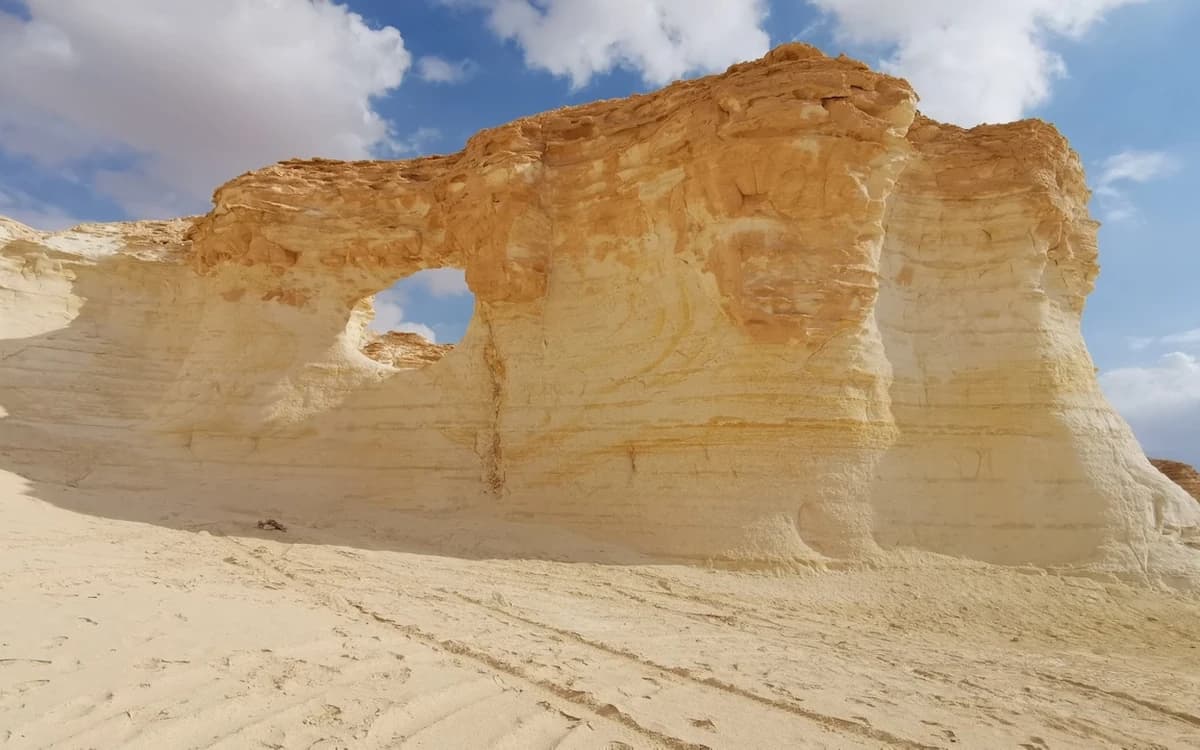 Wind-shaped rock arch in Jordan's White Desert with pale cliffs, carved formations, and bright desert light.