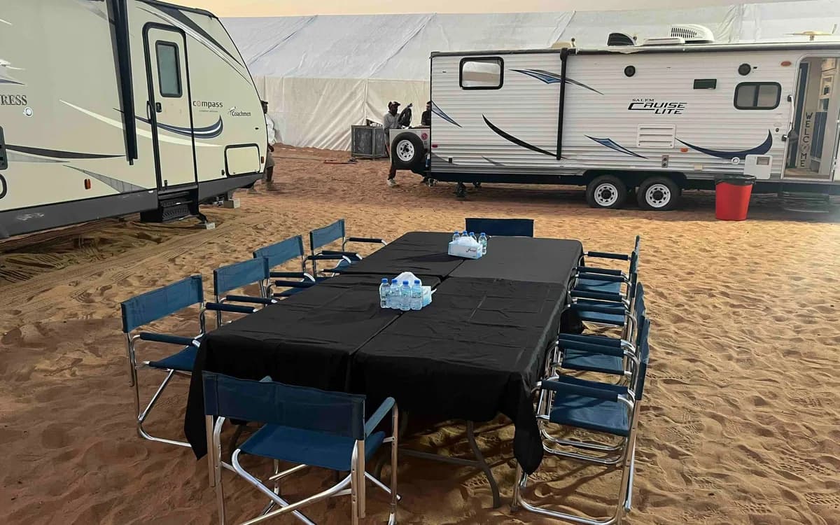 Desert production base camp in Jordan with trailers, crew seating, water, and unit support set up on sand.
