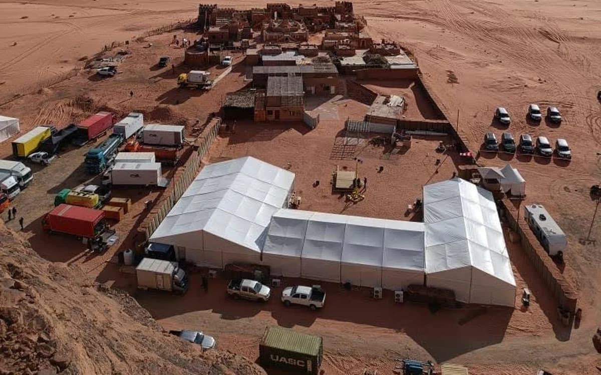 Wide desert unit logistics setup in Jordan with tents, trucks, vehicles, and production support across an open landscape.