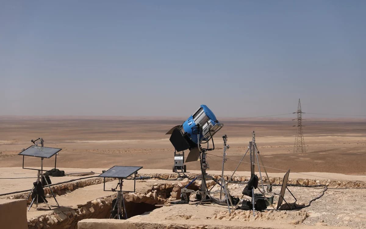 Film lighting and grip equipment set up on a desert overlook in Jordan with stands, reflectors, and a large studio light.
