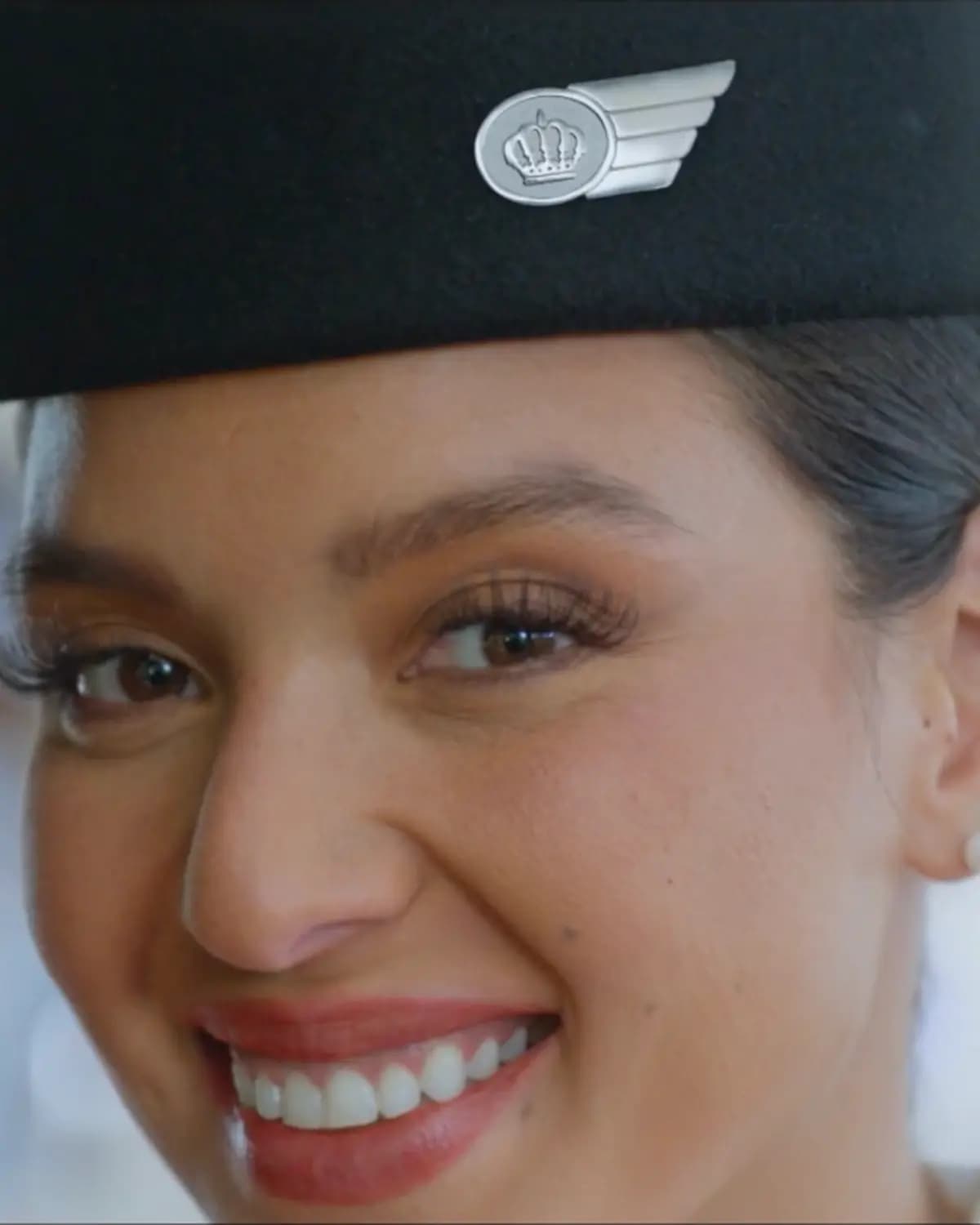 Royal Jordanian Airlines poster showing a close-up of a smiling woman wearing a black cap with a winged emblem.