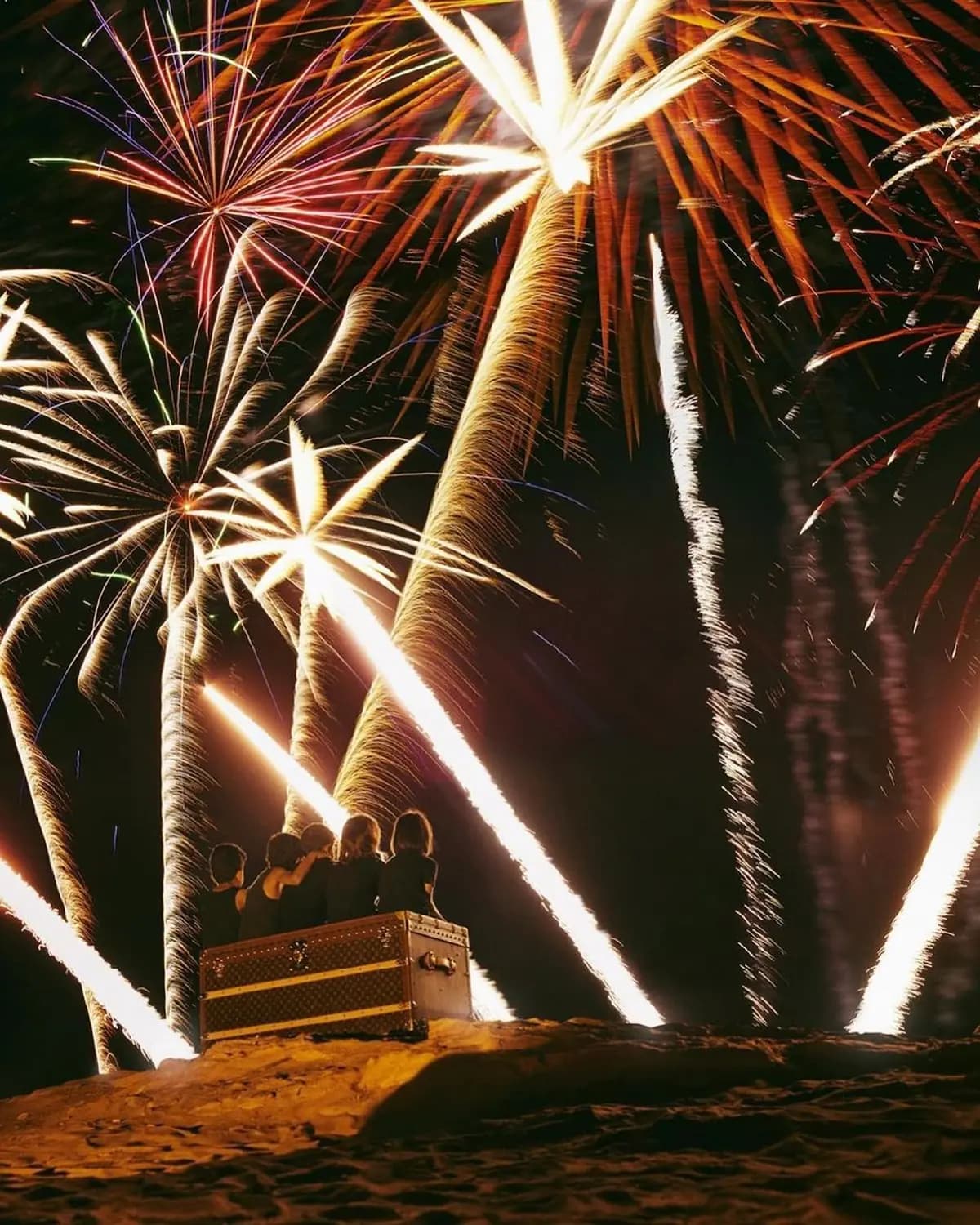 Louis Vuitton poster showing children sitting on a trunk beneath fireworks in a desert night scene.
