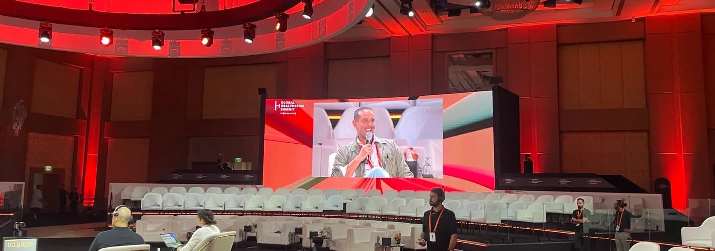 Riyadh summit stage with red lighting, large screen, seating, production crew, and Global Healthspan Summit event branding.