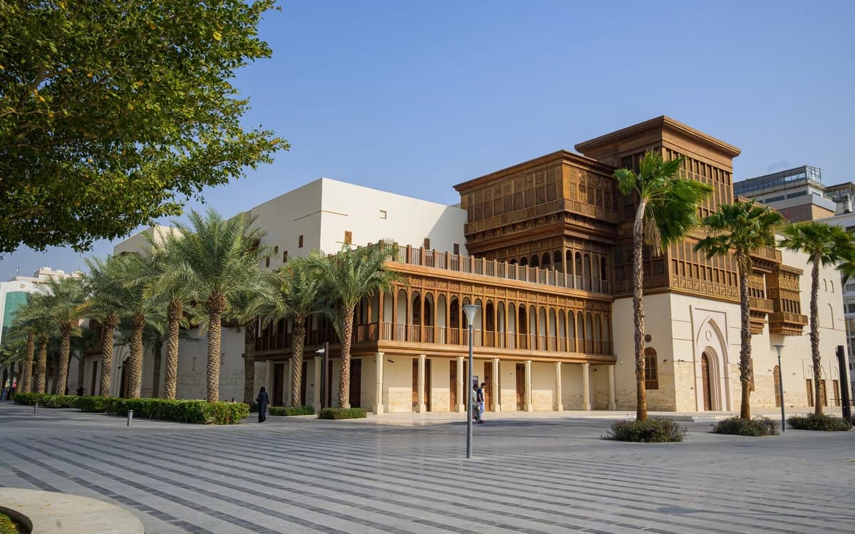 Historic Jeddah street in Saudi Arabia with traditional wooden architecture, palm trees, and a paved public square.