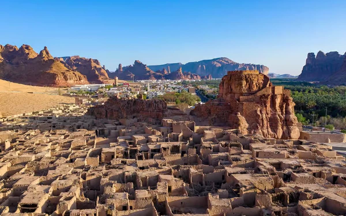 AlUla heritage ruins and oasis in Saudi Arabia with mud-brick structures, palm trees, and sandstone mountains.
