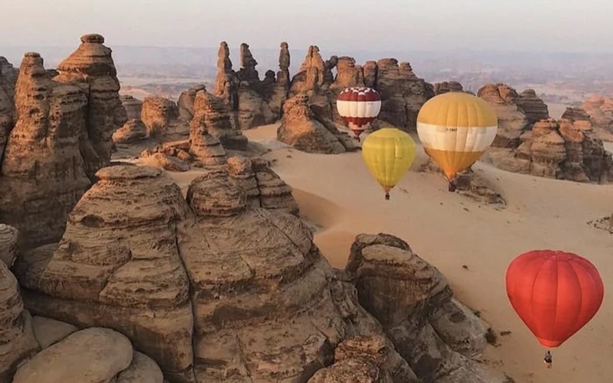 Hot air balloons flying over AlUla sandstone formations and desert valleys in Saudi Arabia.