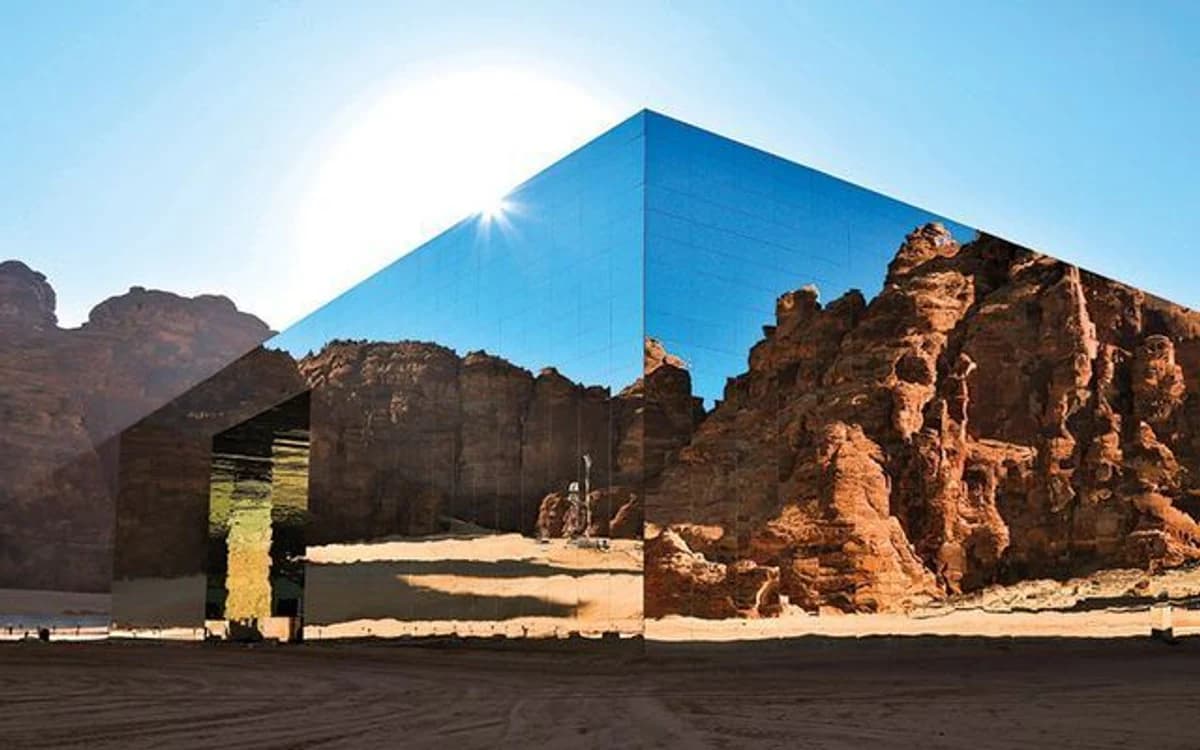 Mirrored Maraya building in AlUla reflecting sandstone cliffs and blue sky in the Saudi desert.