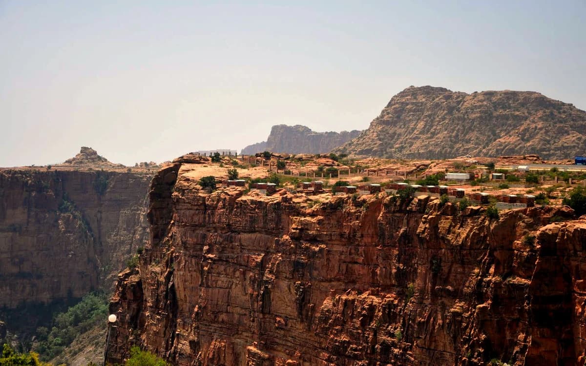 Rocky highland landscape near Abha with sandstone cliffs, mountain backdrop, and structures on the ridge.