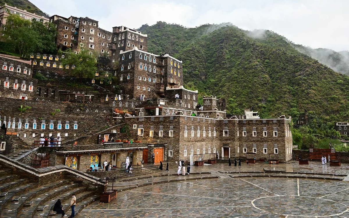 Rijal Almaa heritage village in Saudi Arabia with stone buildings, colourful windows, mountain slopes, and mist.