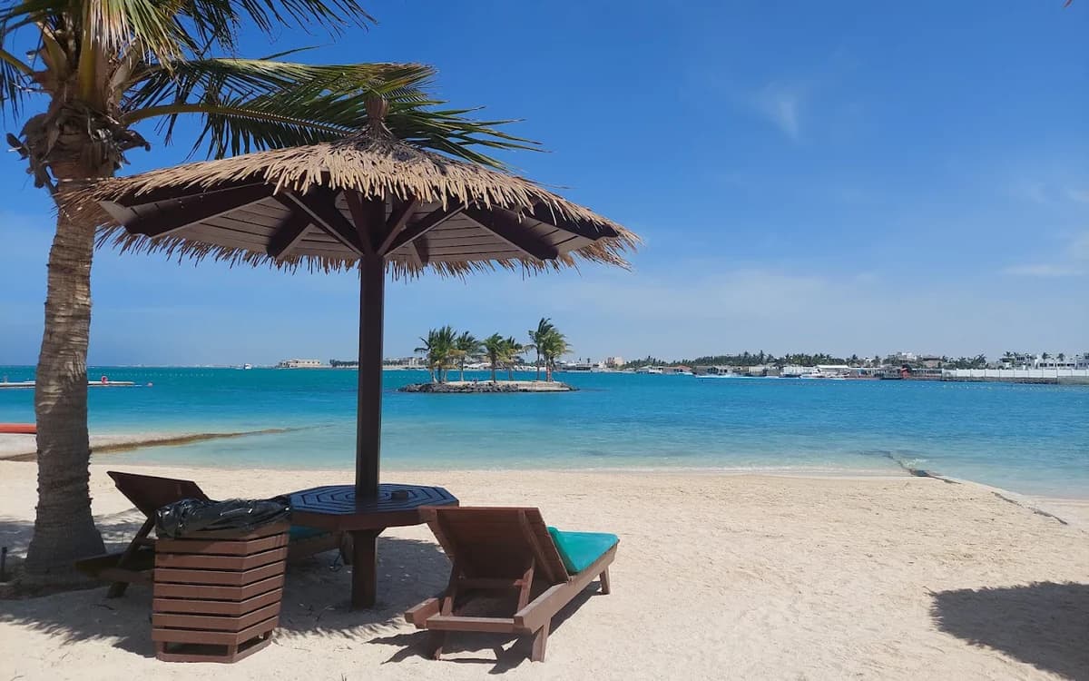Jeddah beach in Saudi Arabia with palm shade, lounge chair, white sand, and turquoise Red Sea water.