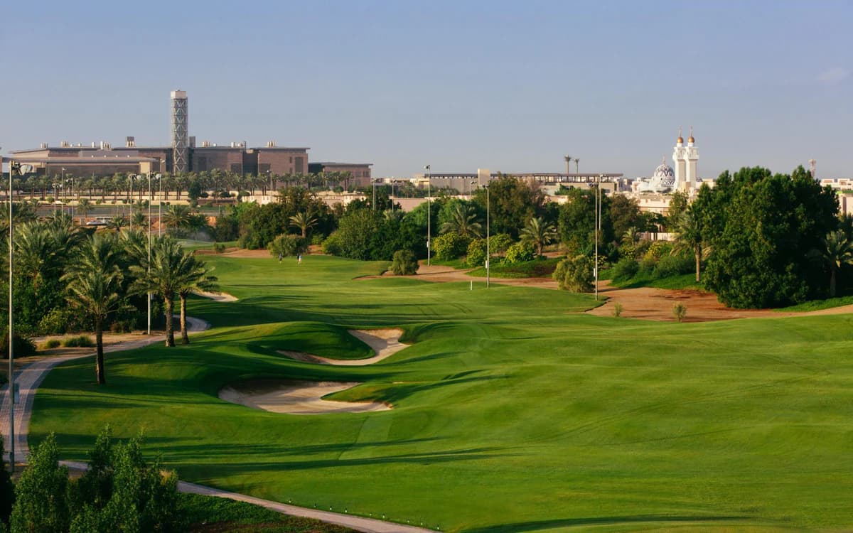 Green golf course in Jeddah with palm trees, sand bunkers, landscaped fairway, and city backdrop.