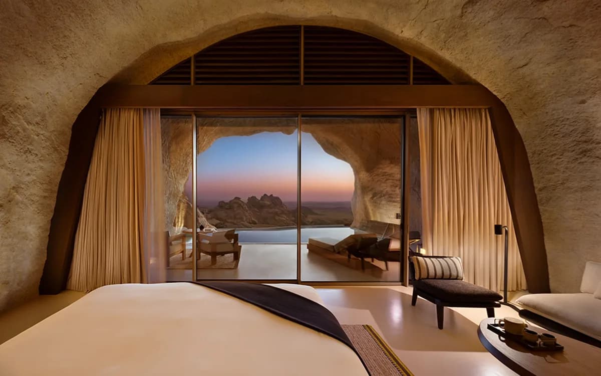 Desert Rock interior in Saudi Arabia with cave-like stone walls, bedroom setting, glass doors, pool terrace, and mountain view.