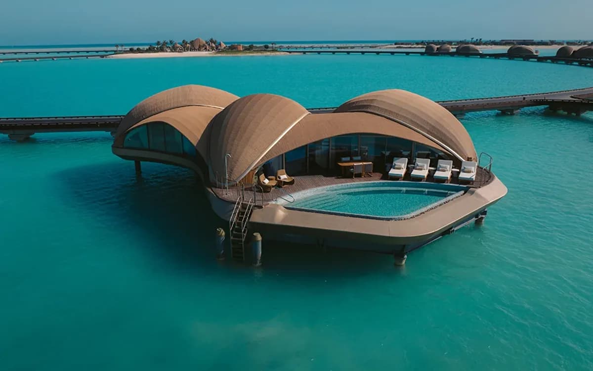 Close view of Shebara Resort overwater villas in the Red Sea at sunset with calm water and curved pod-like structures.