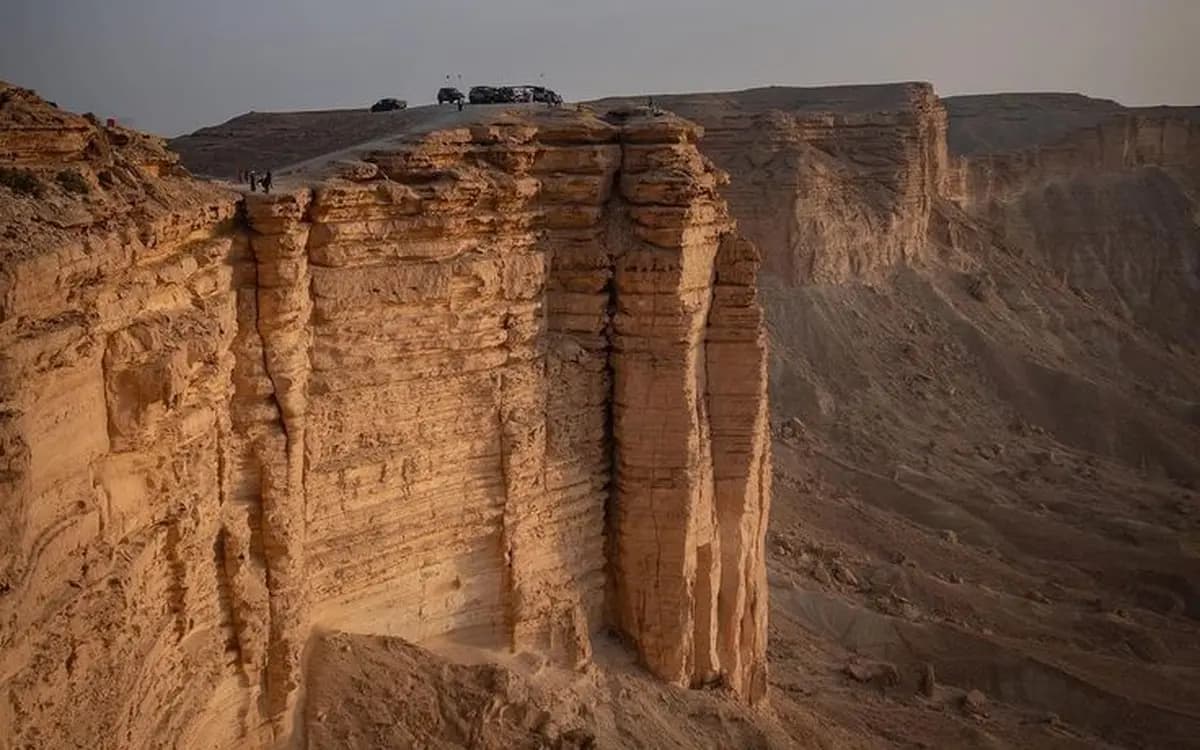 Desert escarpment near Riyadh with sandstone cliffs, canyon landscape, and vehicles parked on the ridge.