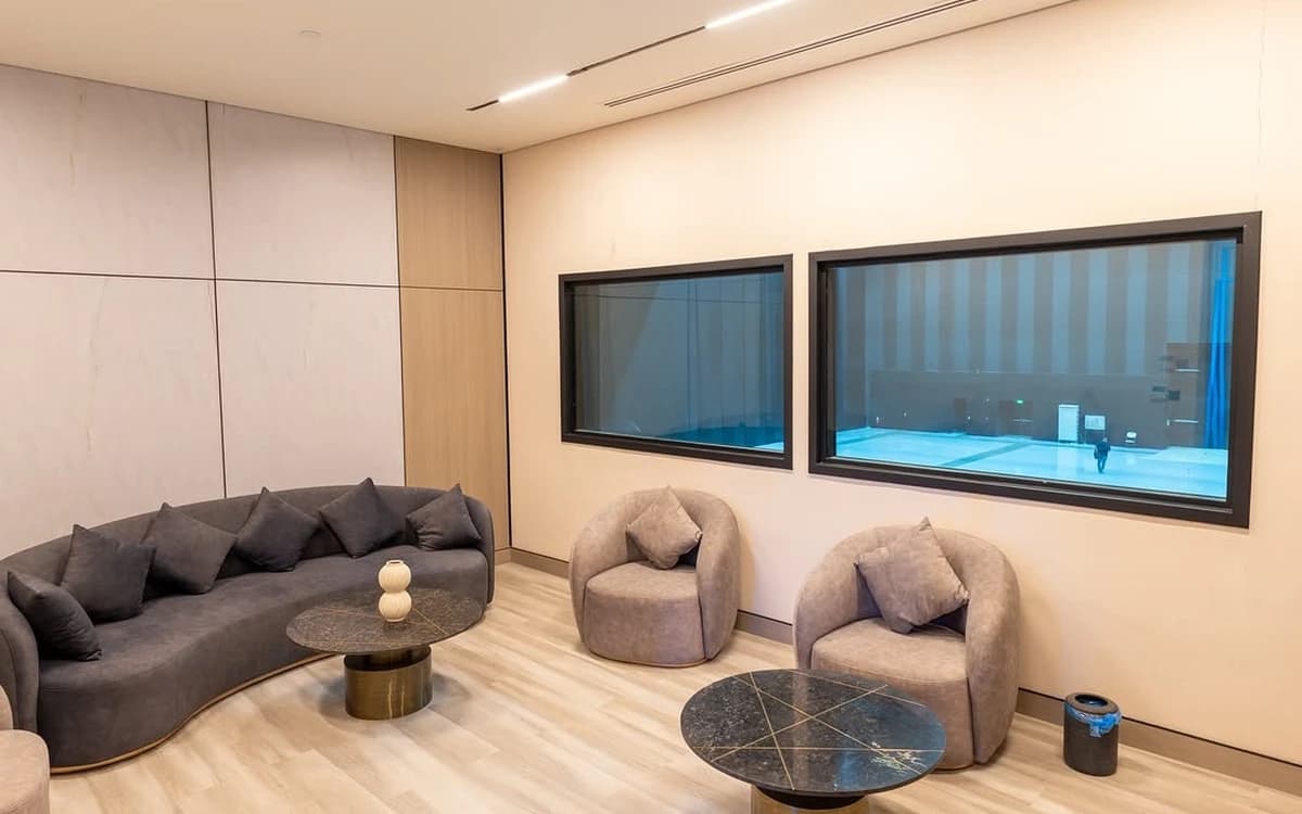 Studio viewing lounge in Saudi Arabia with sofas, tables, interior windows, and controlled production space beyond.