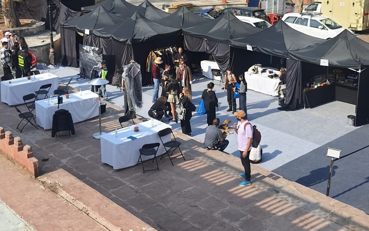 Outdoor production setup in Saudi Arabia with black tents, crew, tables, vehicles, and on-ground shoot support.