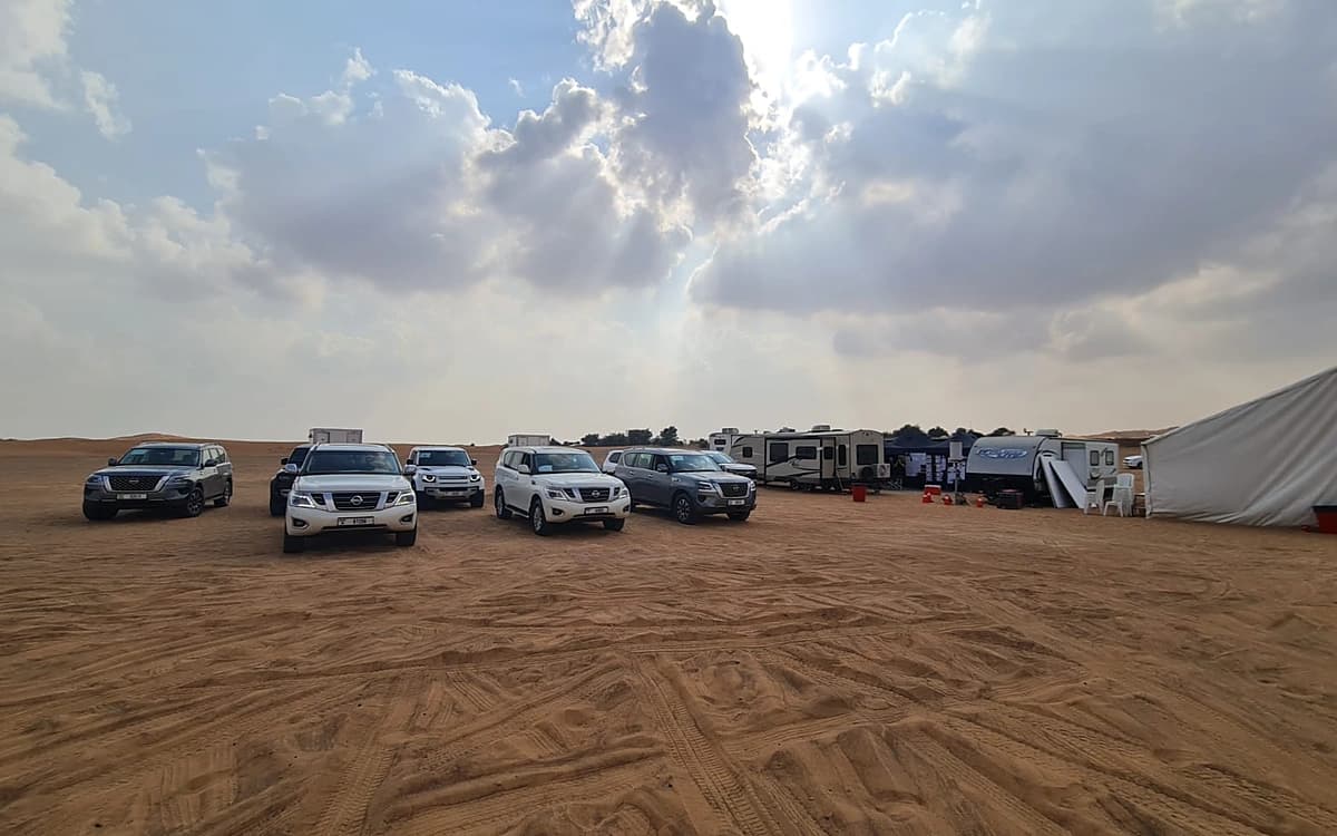 Desert production logistics setup in Saudi Arabia with vehicles, trailers, tents, equipment, and open sand terrain.