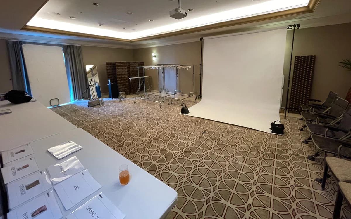 Casting and wardrobe prep room in Saudi Arabia with backdrop, clothing racks, chairs, tables, and printed talent materials.