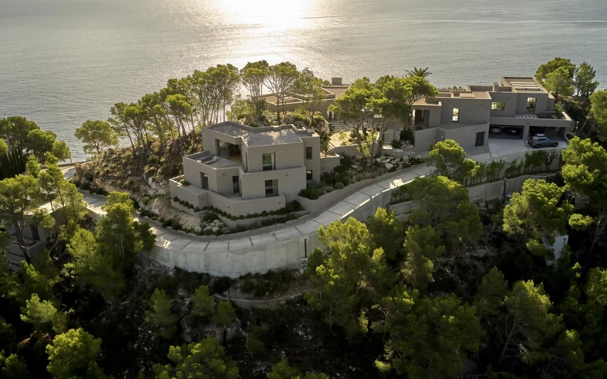 Aerial view of a modern cliffside villa near Alicante with Mediterranean coastline, pine trees, and sea light.