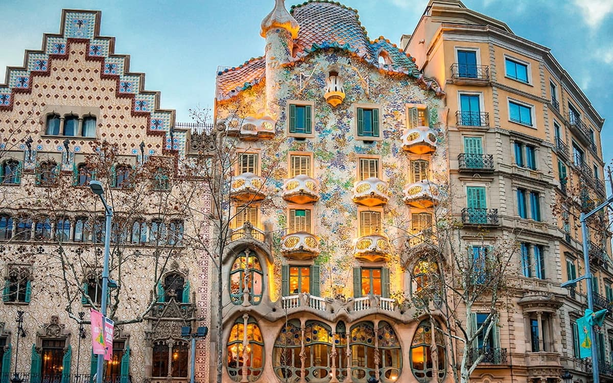 Casa Batlló facade in Barcelona's Eixample district with colourful modernist architecture, balconies, tiled roof, and city street frontage.