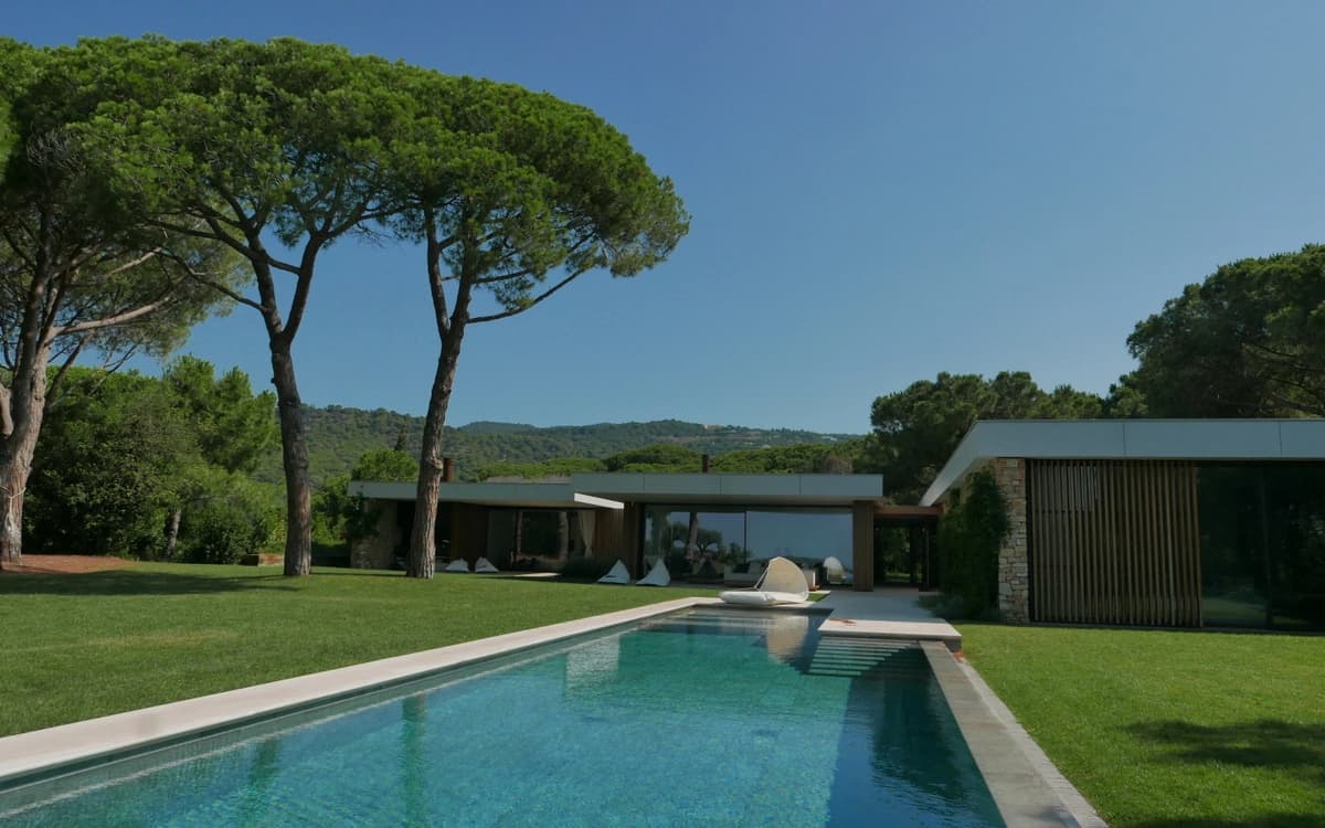 Modern private villa estate in Catalonia with swimming pool, lawn, pine trees, and contemporary exterior architecture.