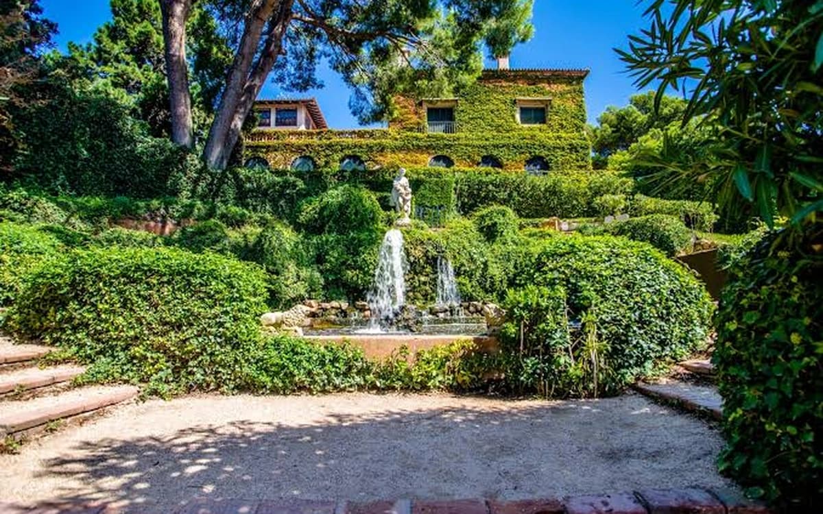 Santa Clotilde Gardens in Lloret de Mar with fountain, hedges, pine trees, and villa exterior in a Mediterranean garden setting.