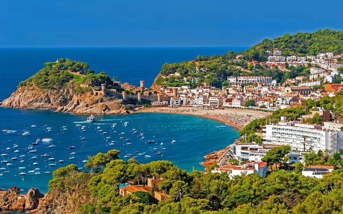 Tossa de Mar coastline on the Costa Brava with castle walls, sandy bay, boats, hillside town, and blue sea.
