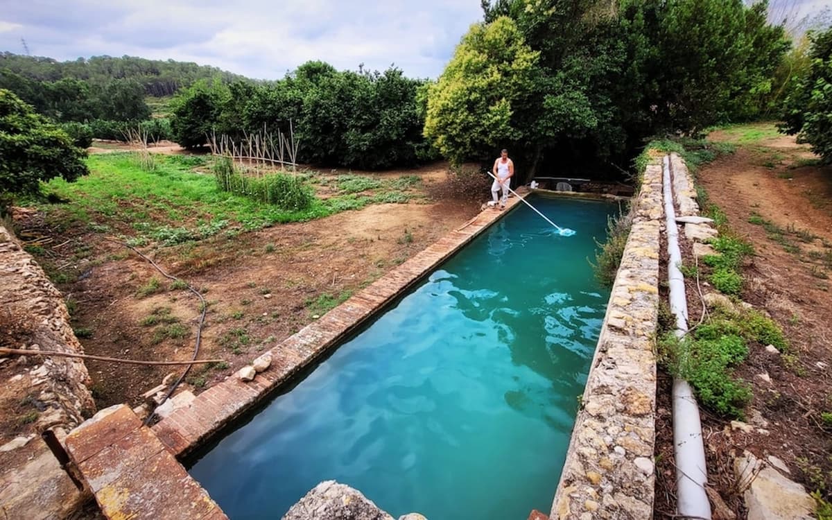 Stone water reservoir at Cosido Farm in Tarragona with turquoise water, garden paths, trees, and rural estate ground.