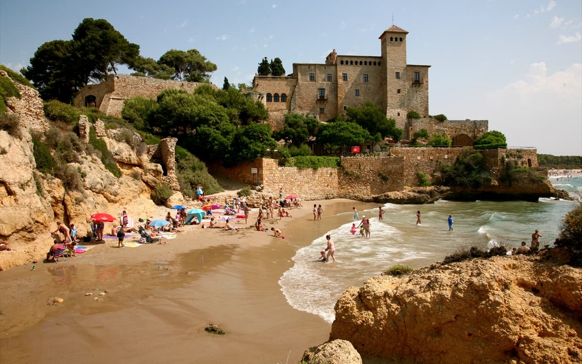 Tamarit Castle near Tarragona above a sandy beach with rocky coast, sea water, and summer beach activity.