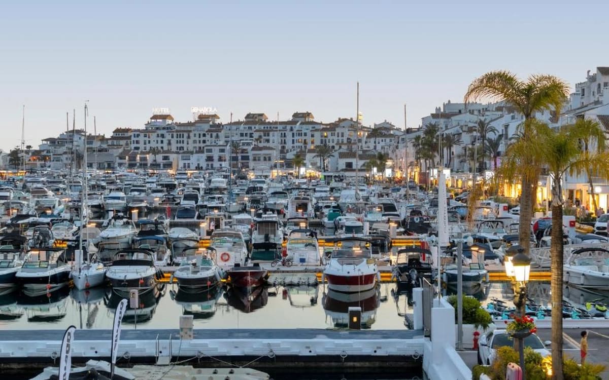 Puerto Banús marina in Marbella, Andalusia with yachts, harbour lights, waterfront buildings, palm trees, and evening atmosphere.