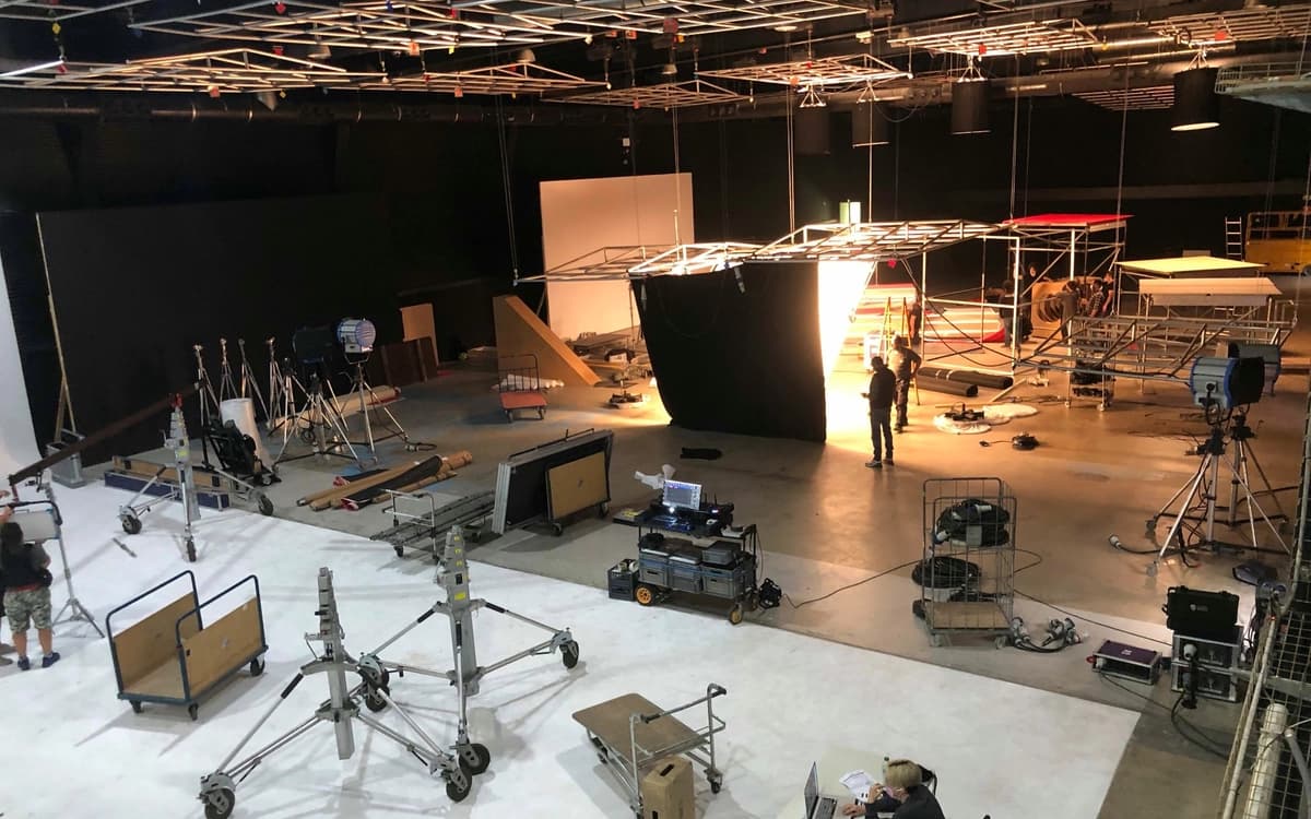 Studio production stage in Barcelona with lighting rigs, set construction, stands, cables, crew, and technical equipment.