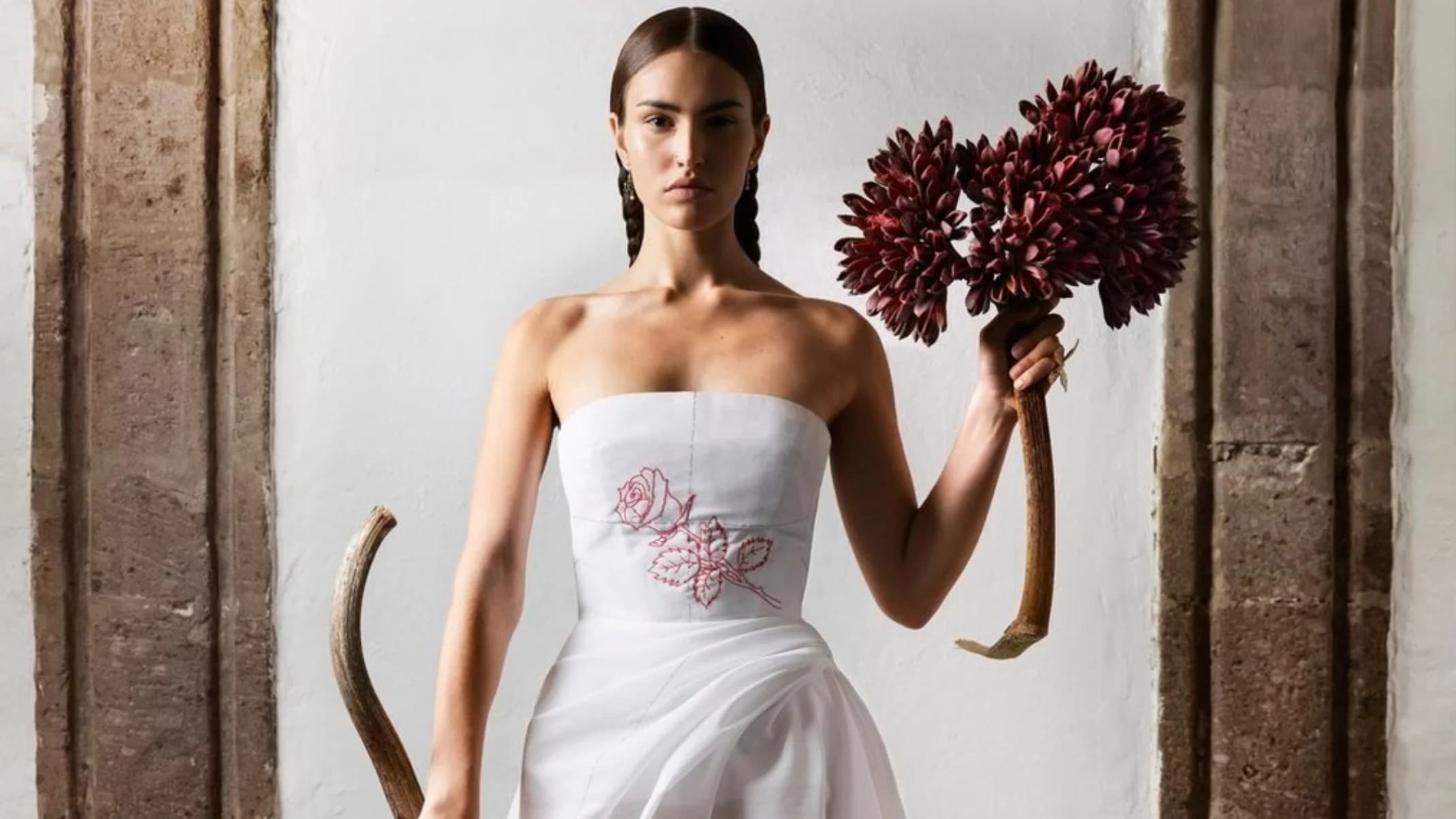 Dior Magazine Issue #44 portrait of a model in a white dress holding red flowers inside a stone interior.